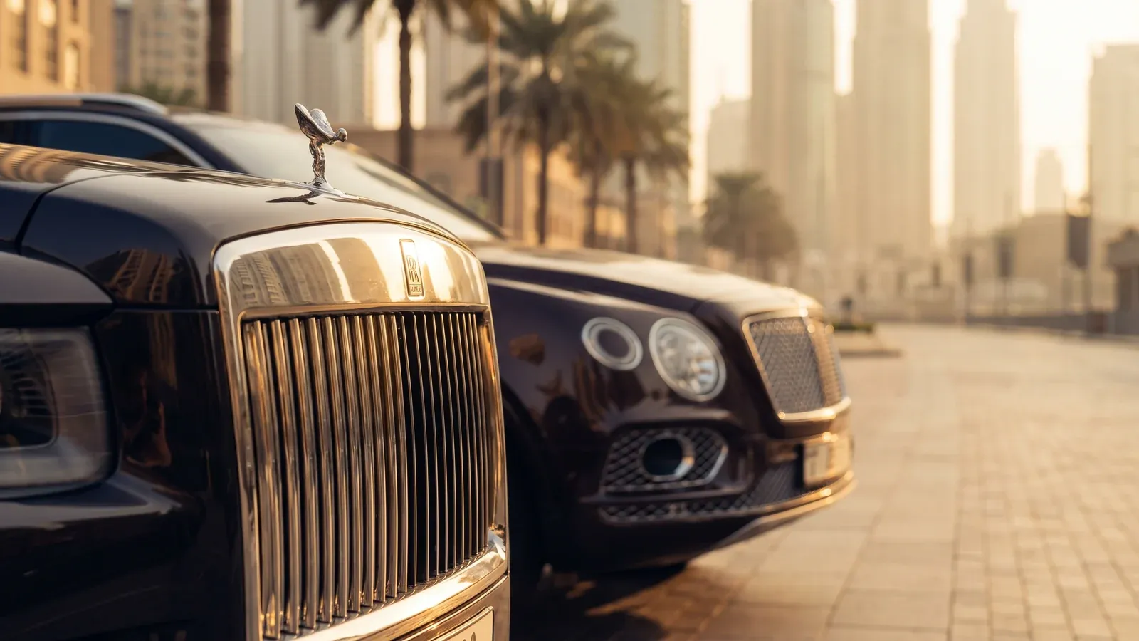 A silver Bentley Bentayga and a black Rolls-Royce Cullinan parked side-by-side near Dubai Creek Harbor.