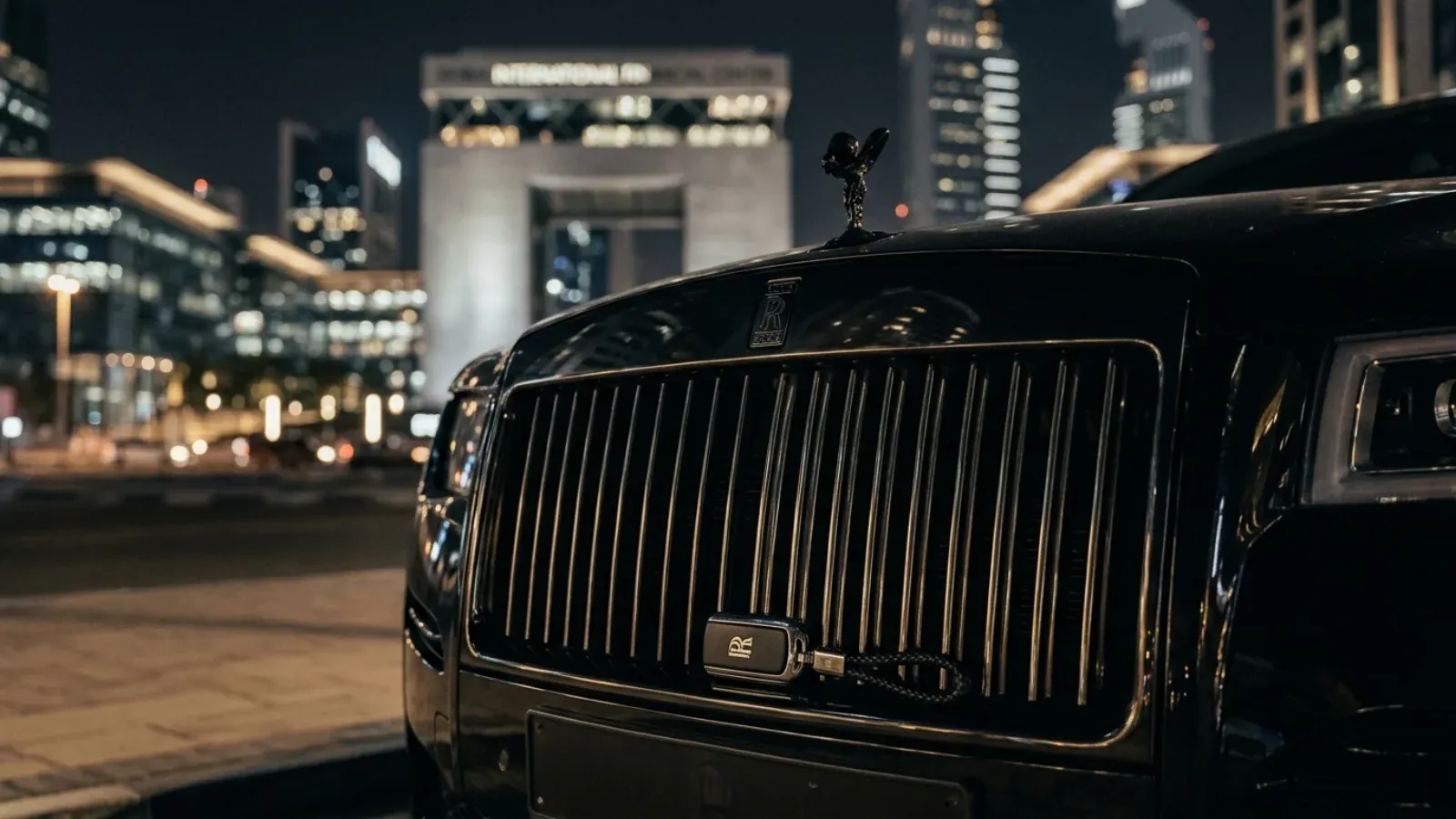 The sleek, dark silhouette of a Rolls-Royce Ghost Black Badge parked under Dubai's city lights