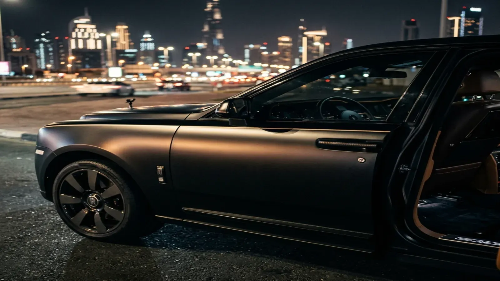 A matte black Rolls-Royce Cullinan parked outside a luxury venue in Dubai Marina at night.